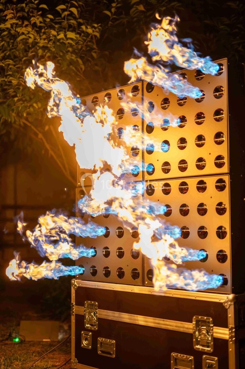 Colonnes de panneaux métalliques perforés émettant des flammes dans un environnement extérieur nocturne.