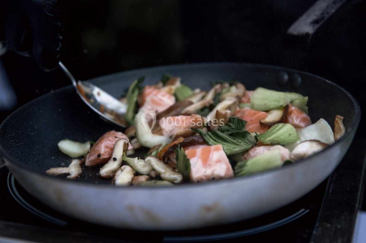 Légumes sautés et morceaux de saumon cuits dans une poêle, remués avec une cuillère en métal.