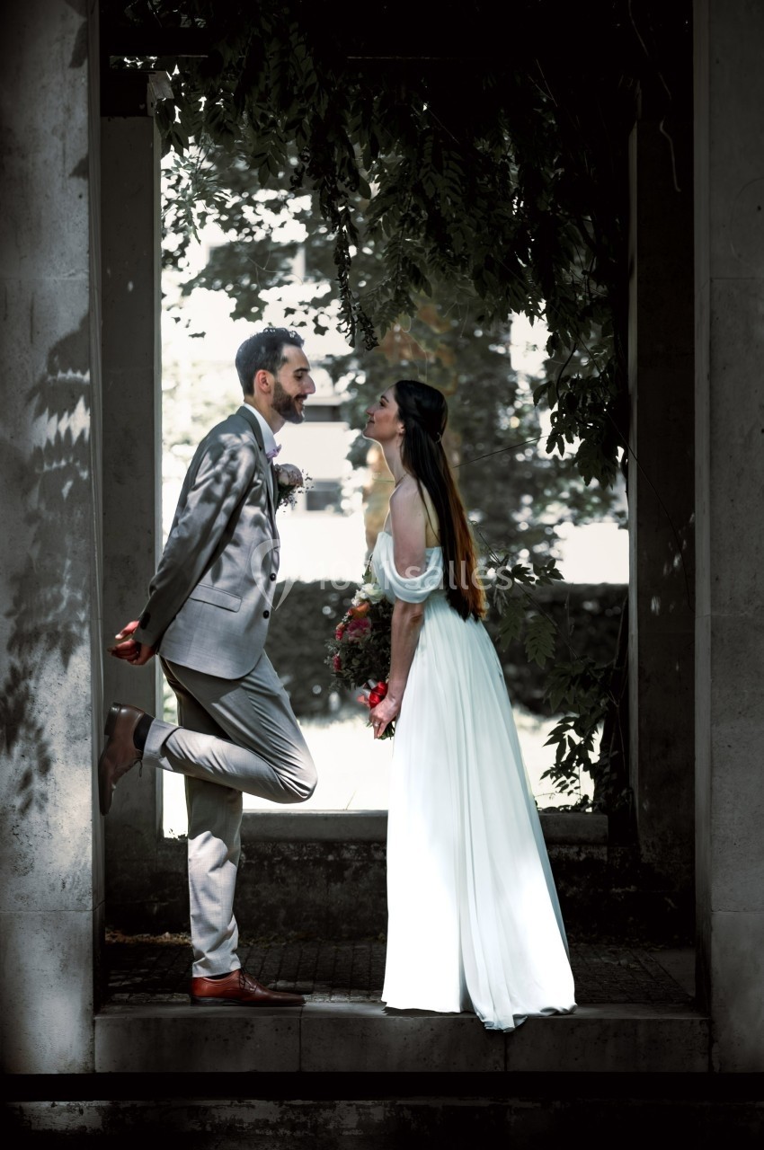 Un couple en tenue de mariage se regarde sous une arche entourée de verdure.