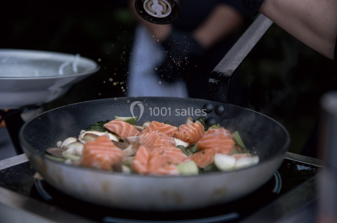 Filets de saumon frais cuisant dans une poêle avec des légumes, saupoudrés d'épices.