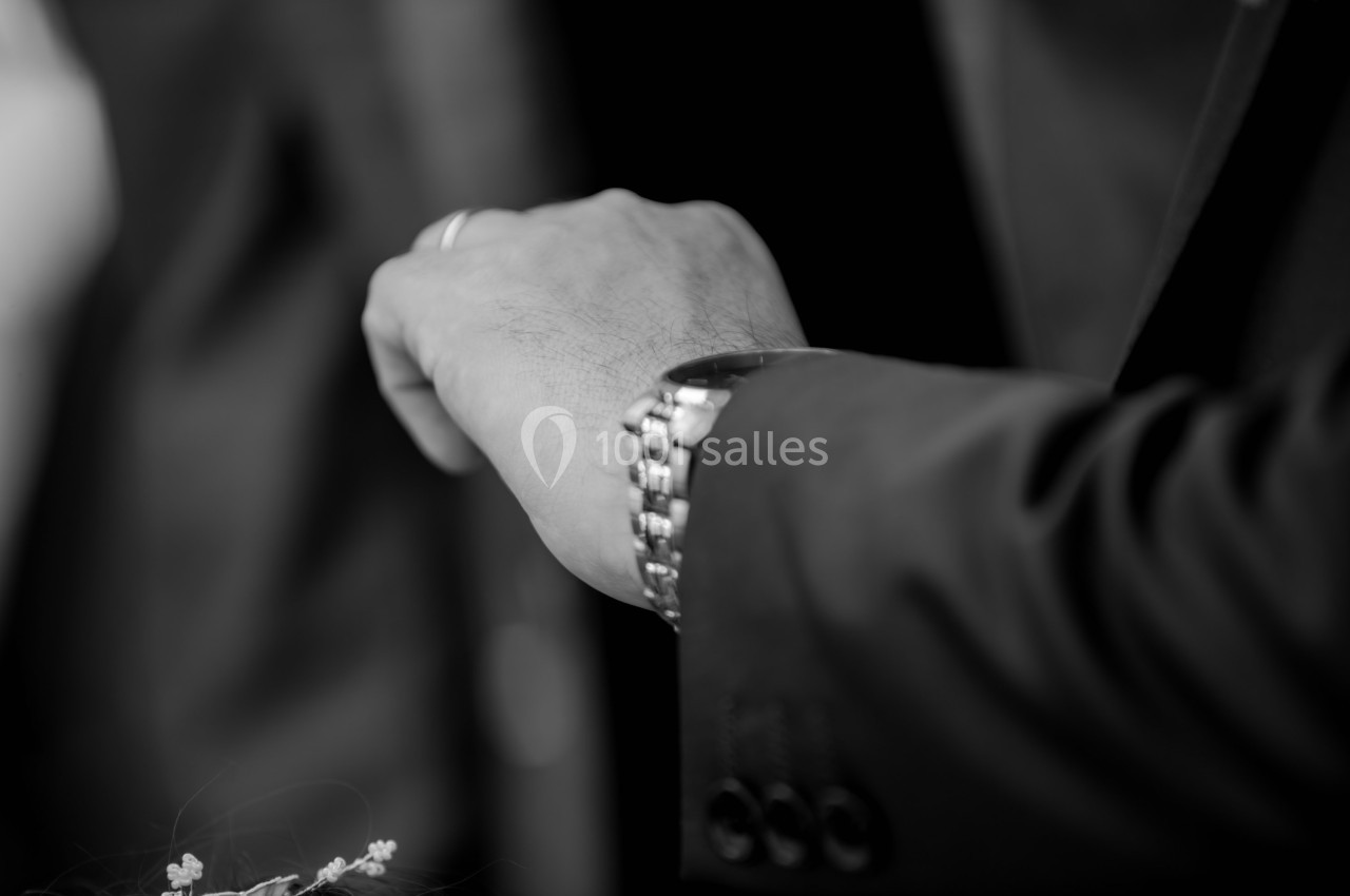 Main d'une personne en costume portant une montre-bracelet, avec un fond sombre flou.