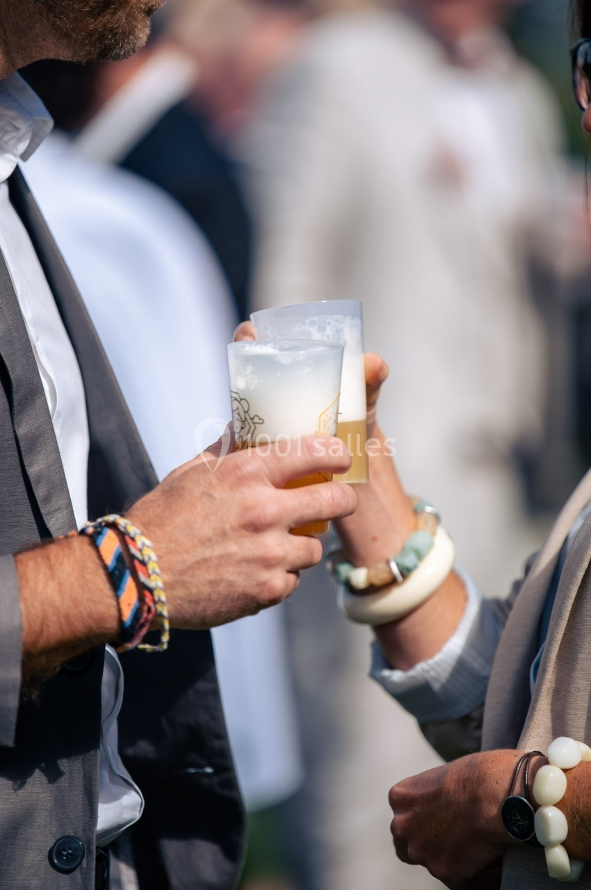 Deux personnes trinquent avec des verres de bière dans un cadre extérieur flou.