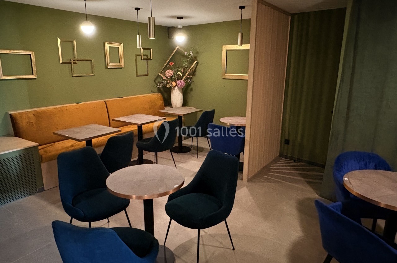 Salle de restaurant moderne avec murs verts, banquette jaune, chaises bleues et tables rondes en bois clair.