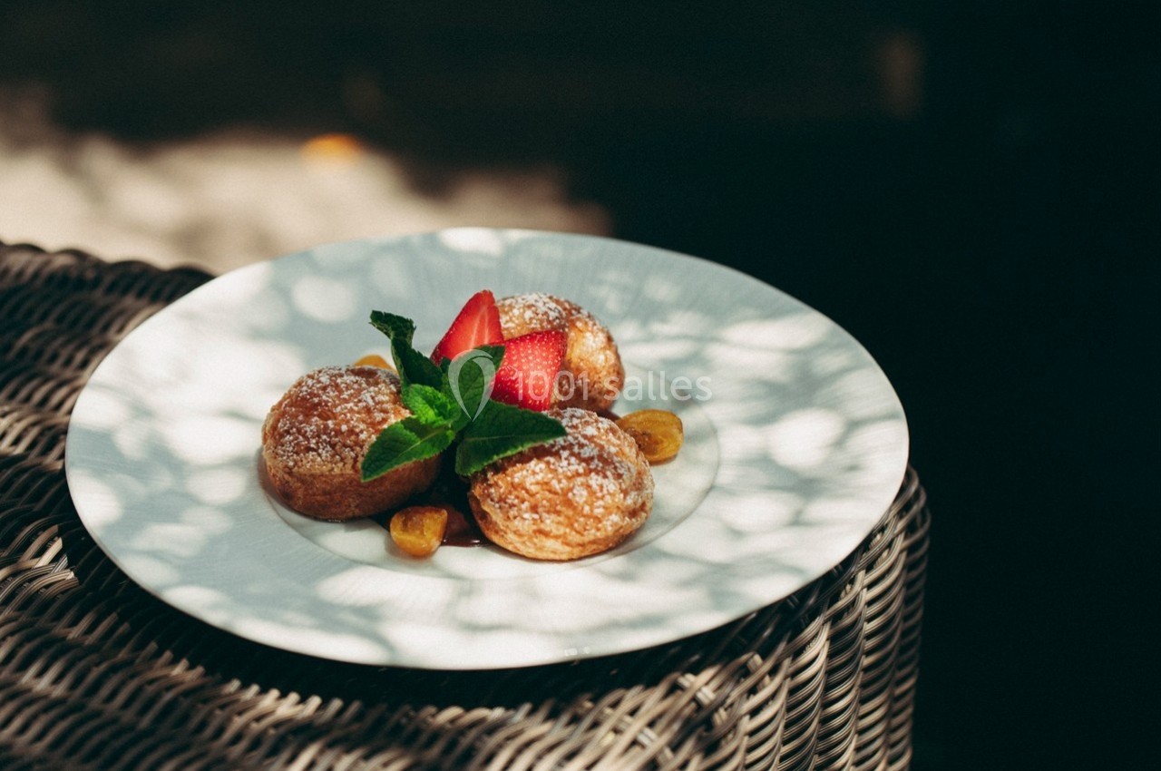 Assiette de beignets saupoudrés de sucre glace, garnis de fraises, feuilles de menthe et morceaux de fruits.
