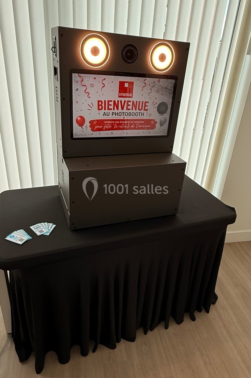 Borne photobooth noire sur une table drapée, avec écran d'accueil lumineux et deux cartes posées à côté.
