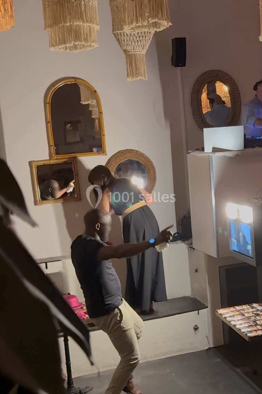 Un homme danse tandis qu'une femme se regarde dans un miroir dans un intérieur décoré de miroirs et de luminaires suspendus.