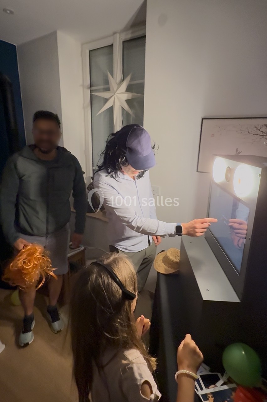 Un homme interagit avec un photobooth lumineux lors d'une fête, entouré de deux autres personnes.