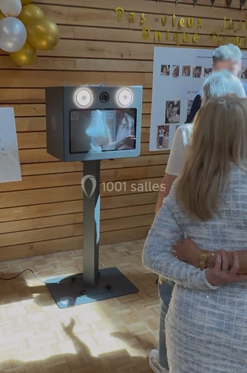 Borne photo interactive dans une salle en bois, entourée de personnes lors d'un événement festif.