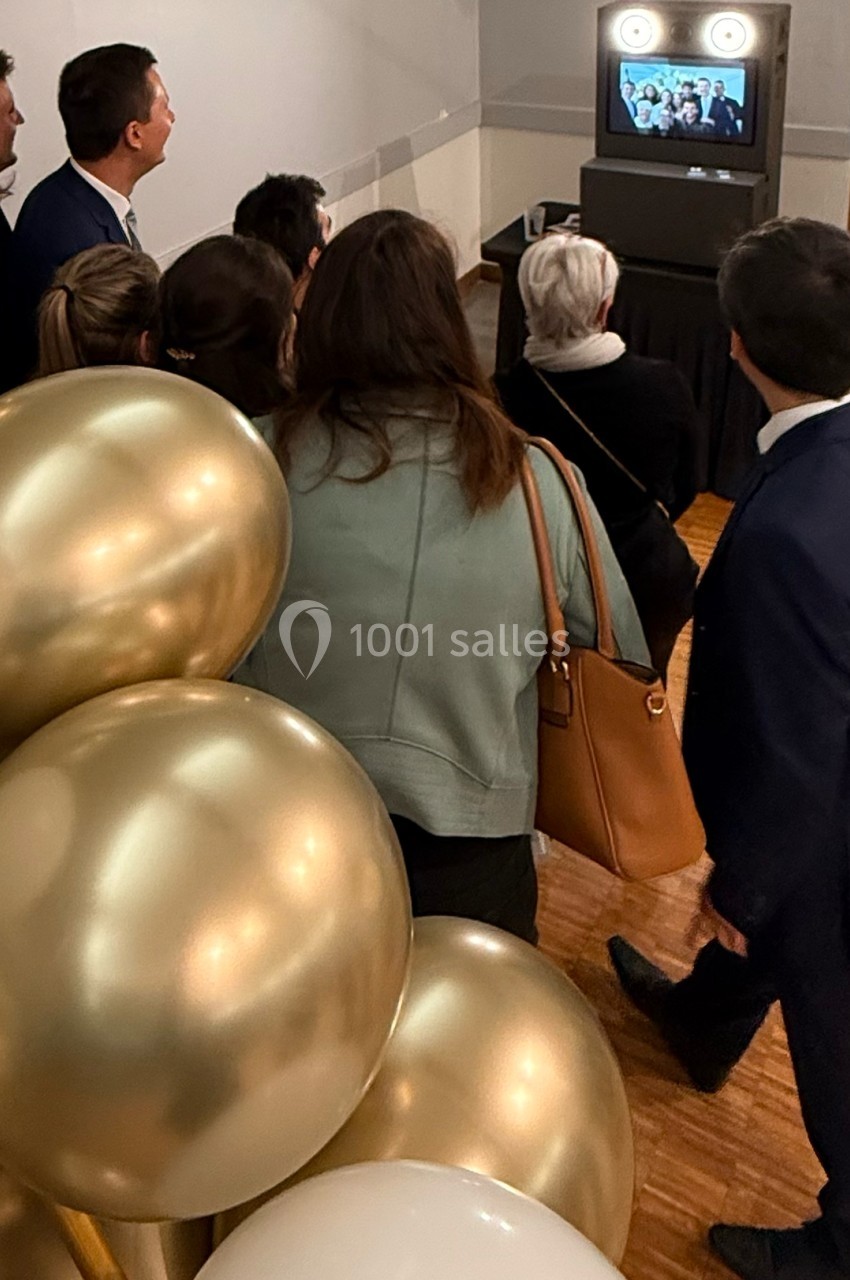 Un groupe de personnes regarde un écran affichant une photo, près d'une décoration avec des ballons dorés.
