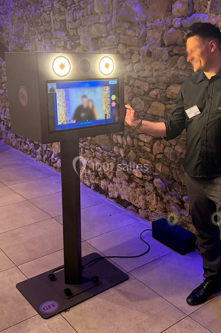 Borne photo interactive avec écran tactile et éclairage intégré, installée dans un espace en pierre éclairé.