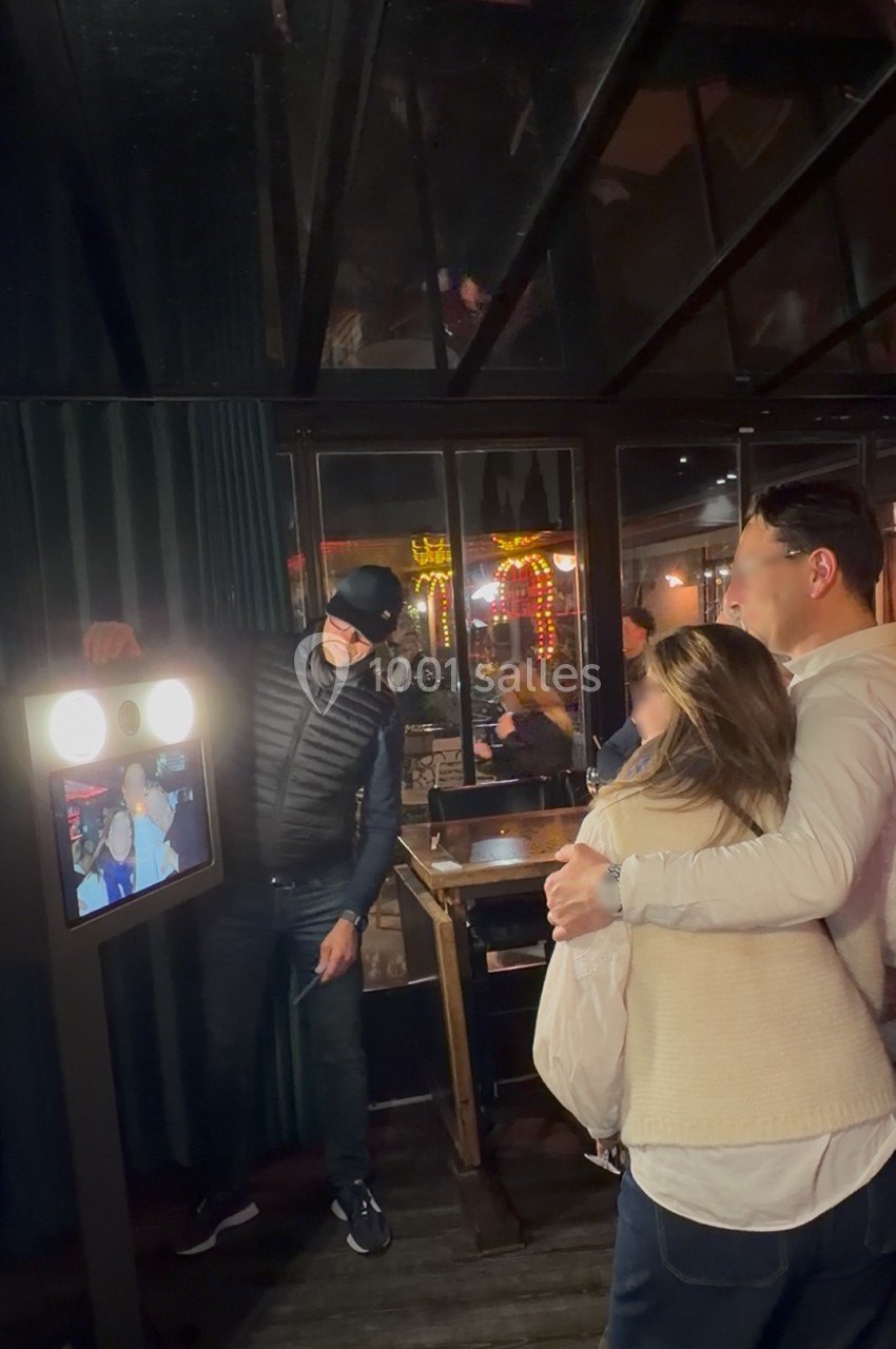 Un couple pose devant une borne photo interactive dans un espace intérieur avec des lumières en arrière-plan.