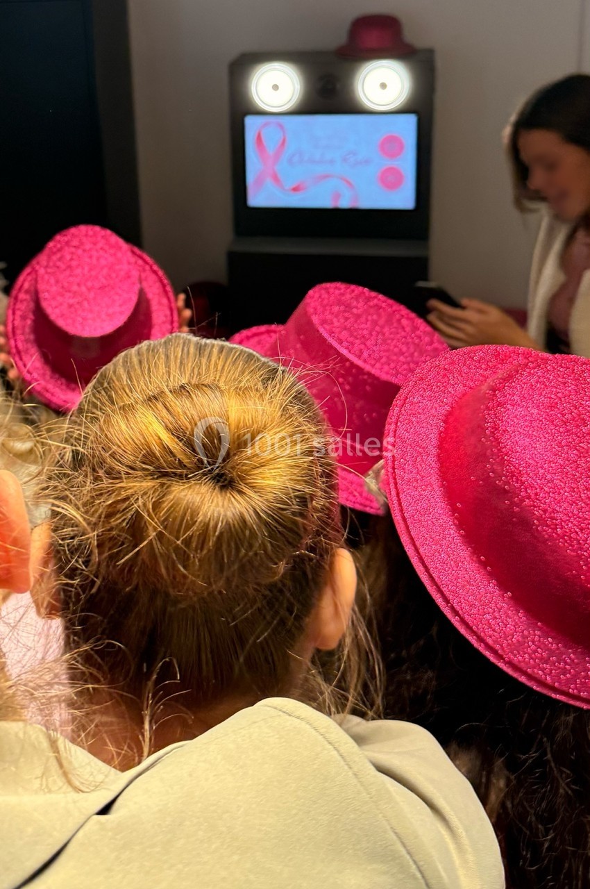 Des personnes portant des chapeaux roses regardent un écran affichant un ruban rose et des éléments graphiques.