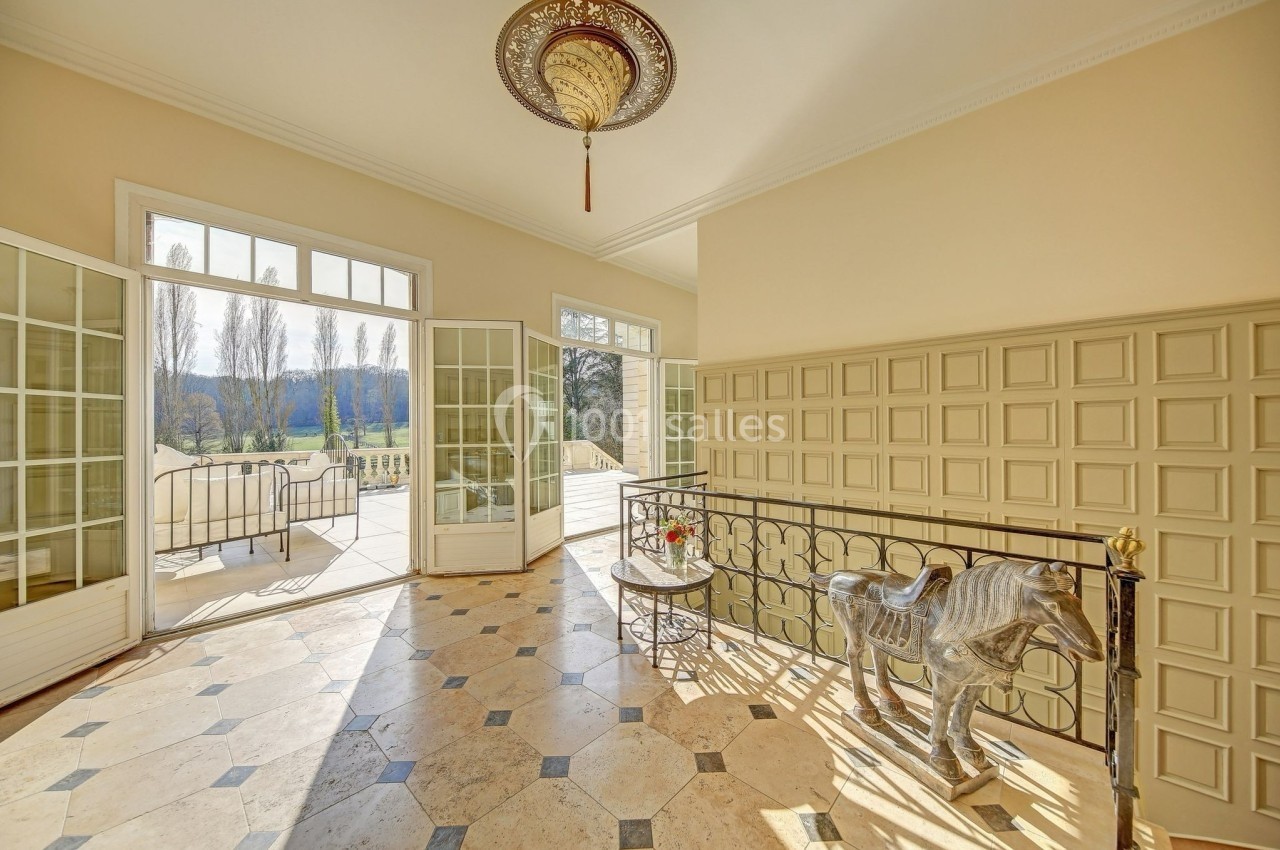 Vue d'un palier lumineux avec sol en marbre, balustrade en métal, sculpture de cheval et accès à une terrasse extérieure.