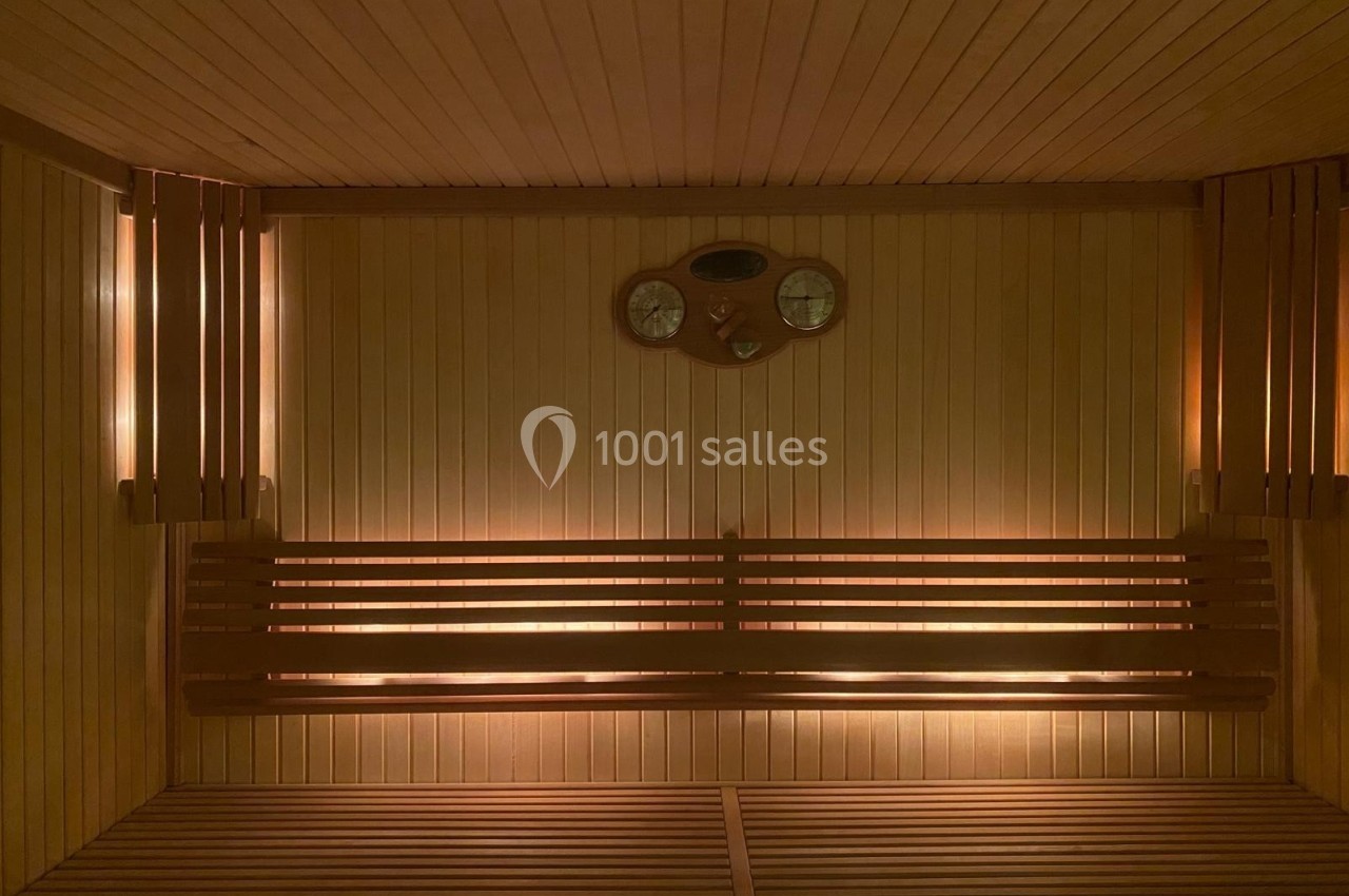 Intérieur d'un sauna en bois avec bancs, éclairage tamisé et thermomètre mural.