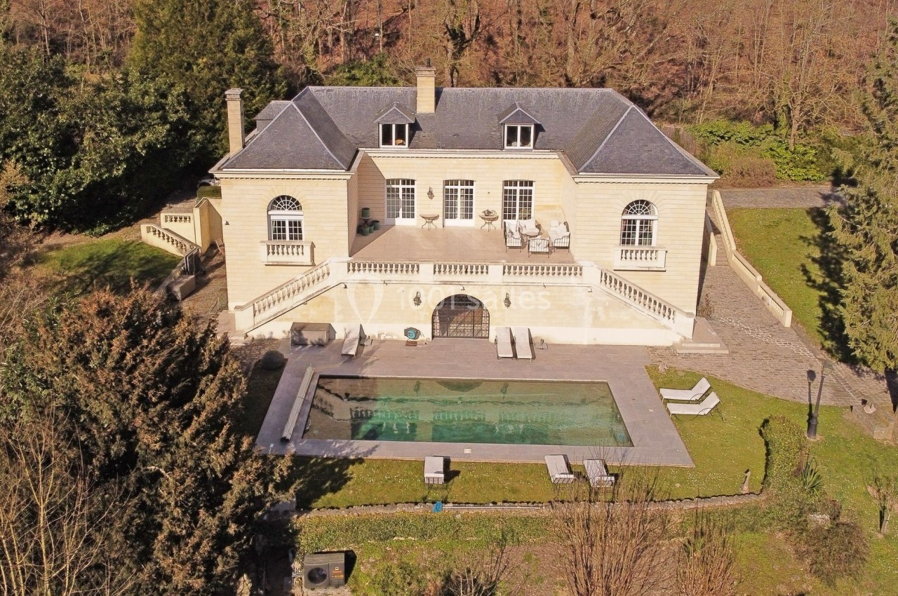 Vue aérienne d'une grande maison en pierre avec piscine, terrasse et jardin arboré en arrière-plan.