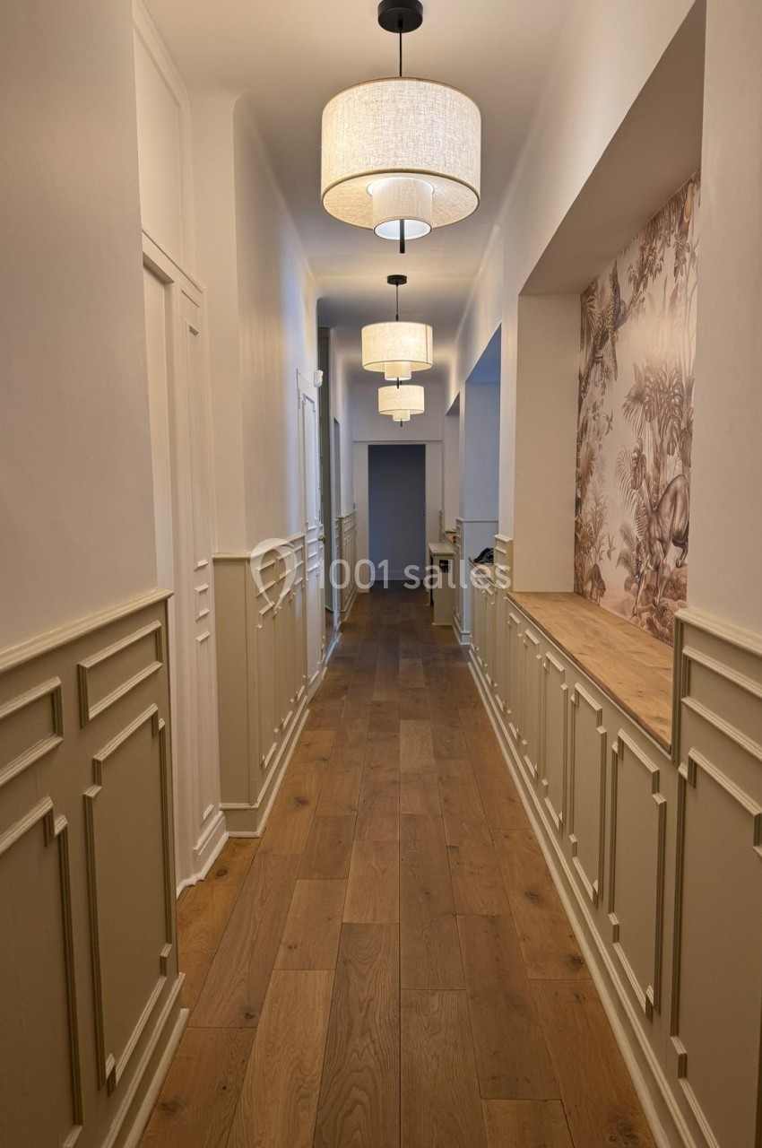 Couloir lumineux avec parquet en bois, murs blancs et beige, moulures classiques et papier peint à motifs végétaux.