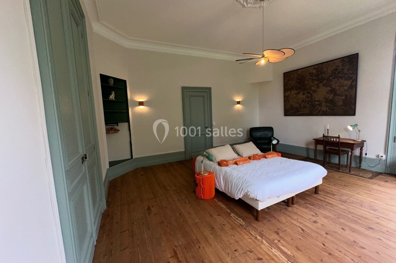 Chambre lumineuse avec lit double, parquet en bois, bureau, fauteuil et décoration murale dans un intérieur épuré.