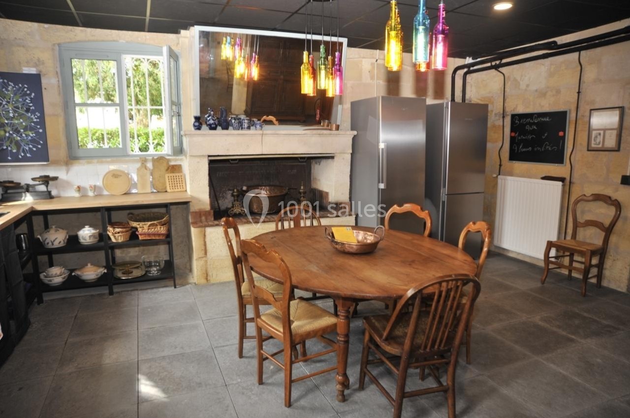 Cuisine rustique avec table en bois, chaises assorties, cheminée ancienne, étagères ouvertes et réfrigérateurs modernes.