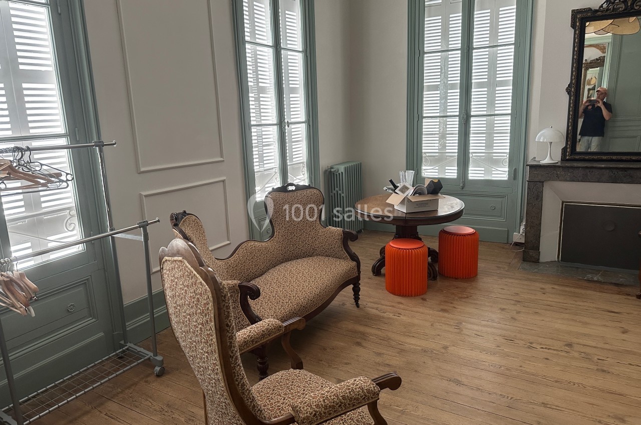 Salon lumineux avec parquet, mobilier ancien, table ronde, tabourets orange et miroir mural.
