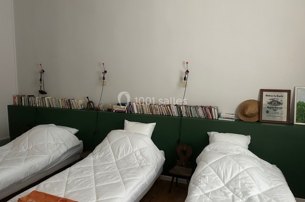 Trois lits simples avec couettes blanches alignés devant une étagère verte remplie de livres et décorations.