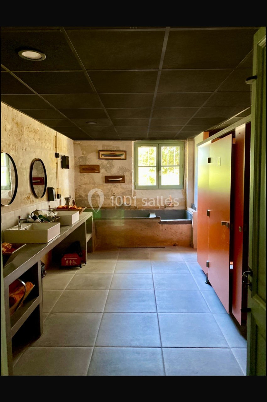 Salle de bain spacieuse avec murs en pierre, deux lavabos, miroirs ronds, baignoire et cabines colorées.
