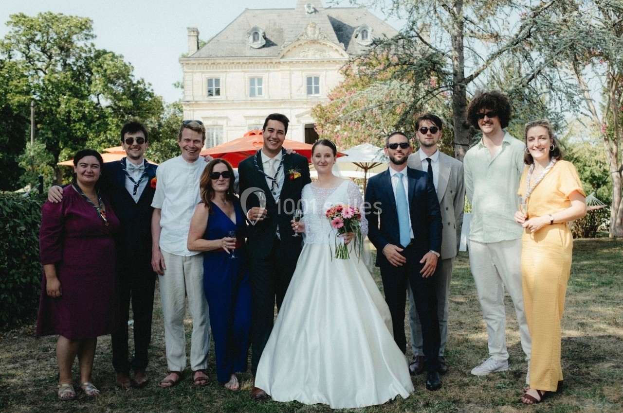Un groupe de personnes posant devant un bâtiment ancien, avec une mariée en robe blanche au centre.