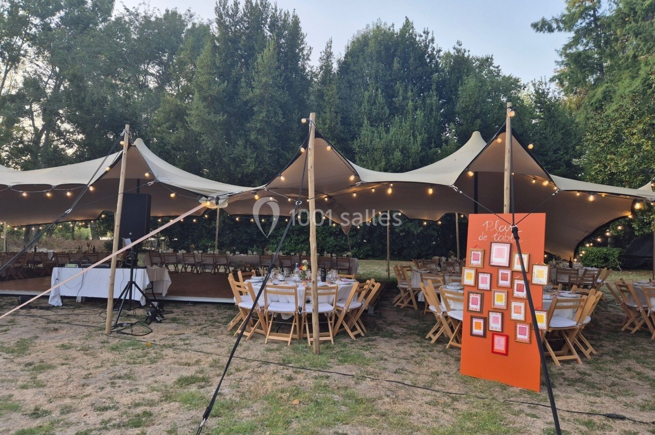 Tente de réception en extérieur avec tables dressées et un panneau de plan de table au premier plan.