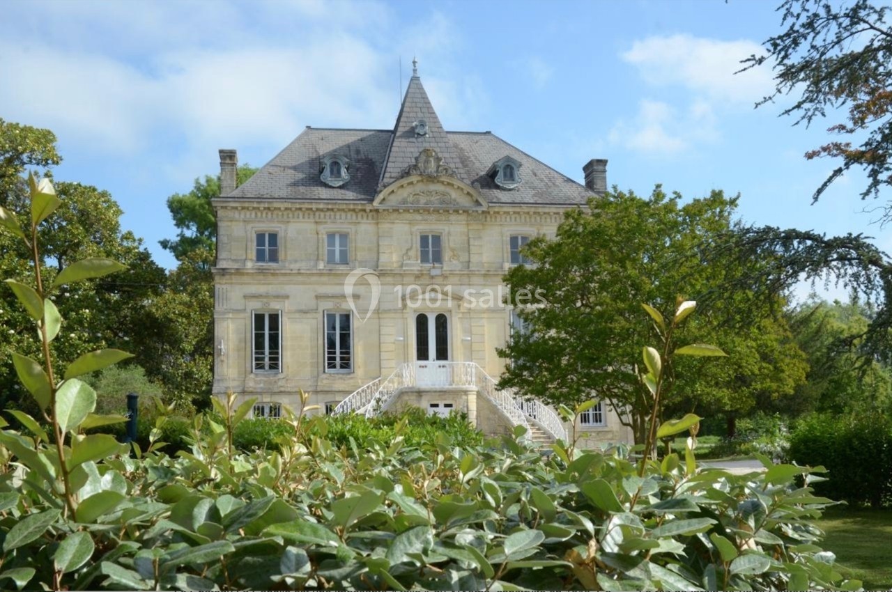 Façade d'un manoir en pierre entouré de verdure, avec un ciel bleu en arrière-plan.