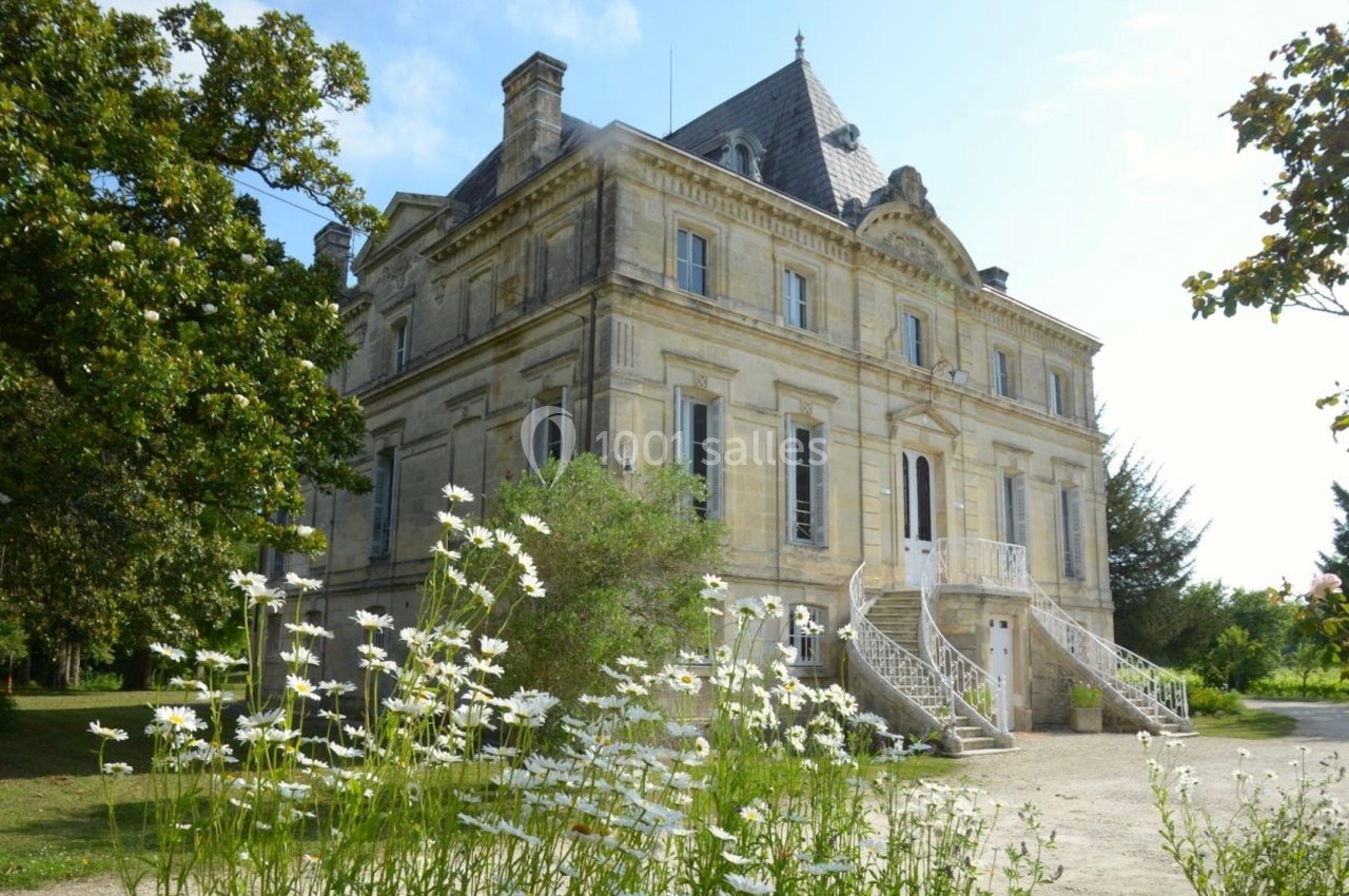 Façade d'un château en pierre entouré de verdure, avec des marguerites au premier plan.
