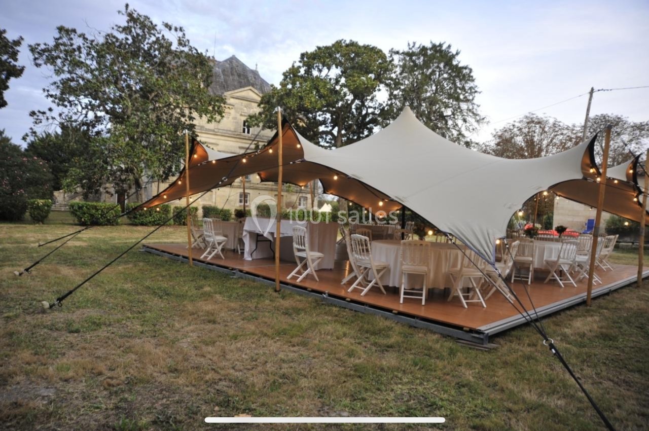 Tente élégante installée en extérieur avec tables et chaises dressées pour un événement, entourée d'arbres.