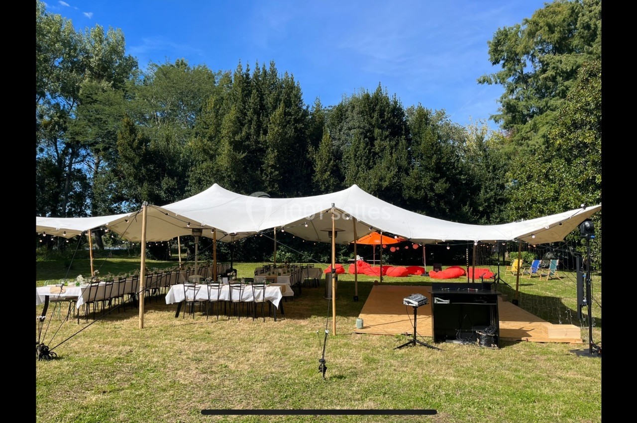 Tente blanche installée dans un jardin, avec tables dressées et espace de réception en plein air.