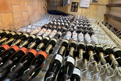 Miniature Location salle Arveyres (Gironde) - Château la Capelle #38 Bouteilles de vin alignées sur des supports métalliques dans une cave aux murs en pierre.