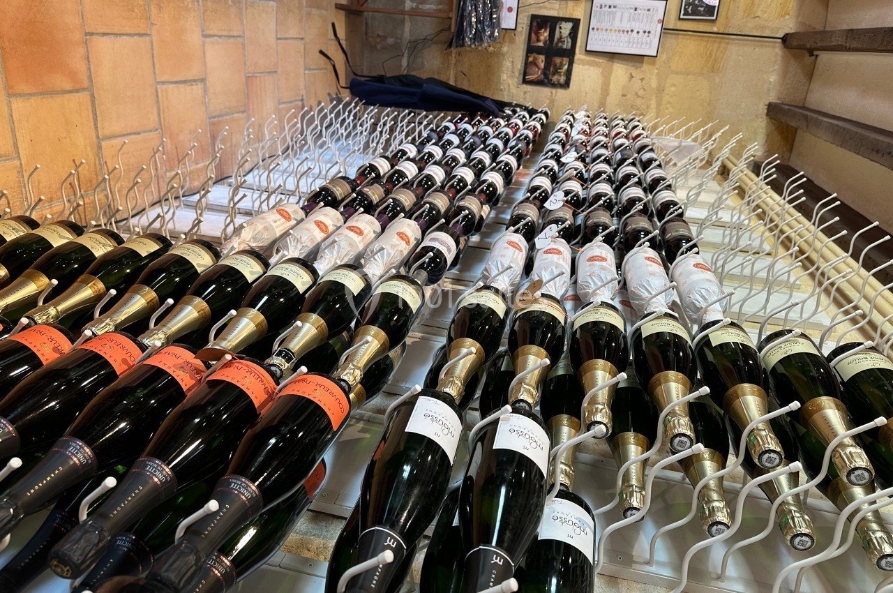Bouteilles de vin alignées sur des supports métalliques dans une cave aux murs en pierre.