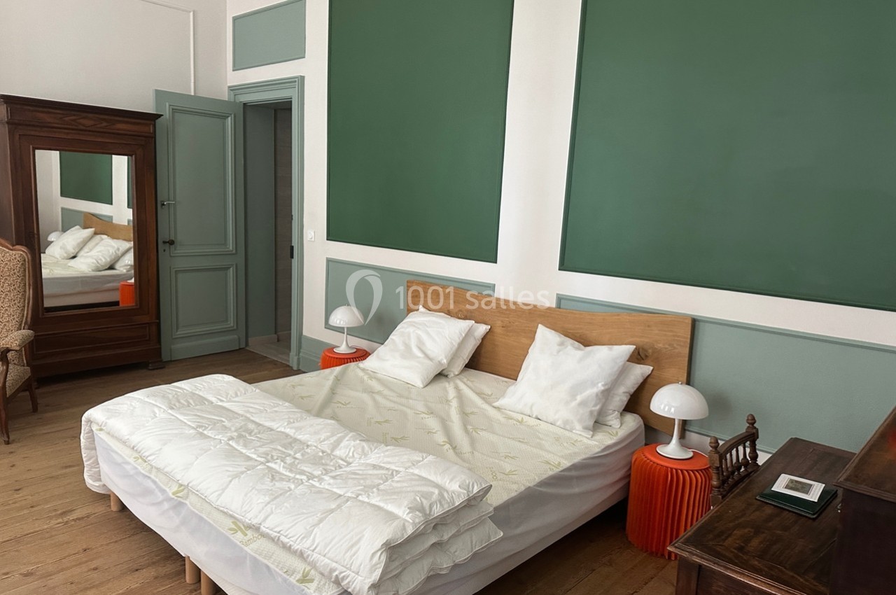 Chambre avec lit double, chevets orange, armoire en bois avec miroir et murs peints en vert et blanc.