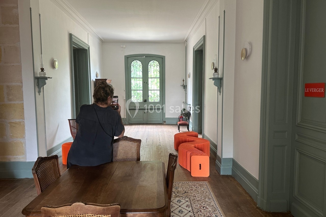 Une femme assise à une table en bois dans une pièce lumineuse avec des murs blancs et des meubles colorés.