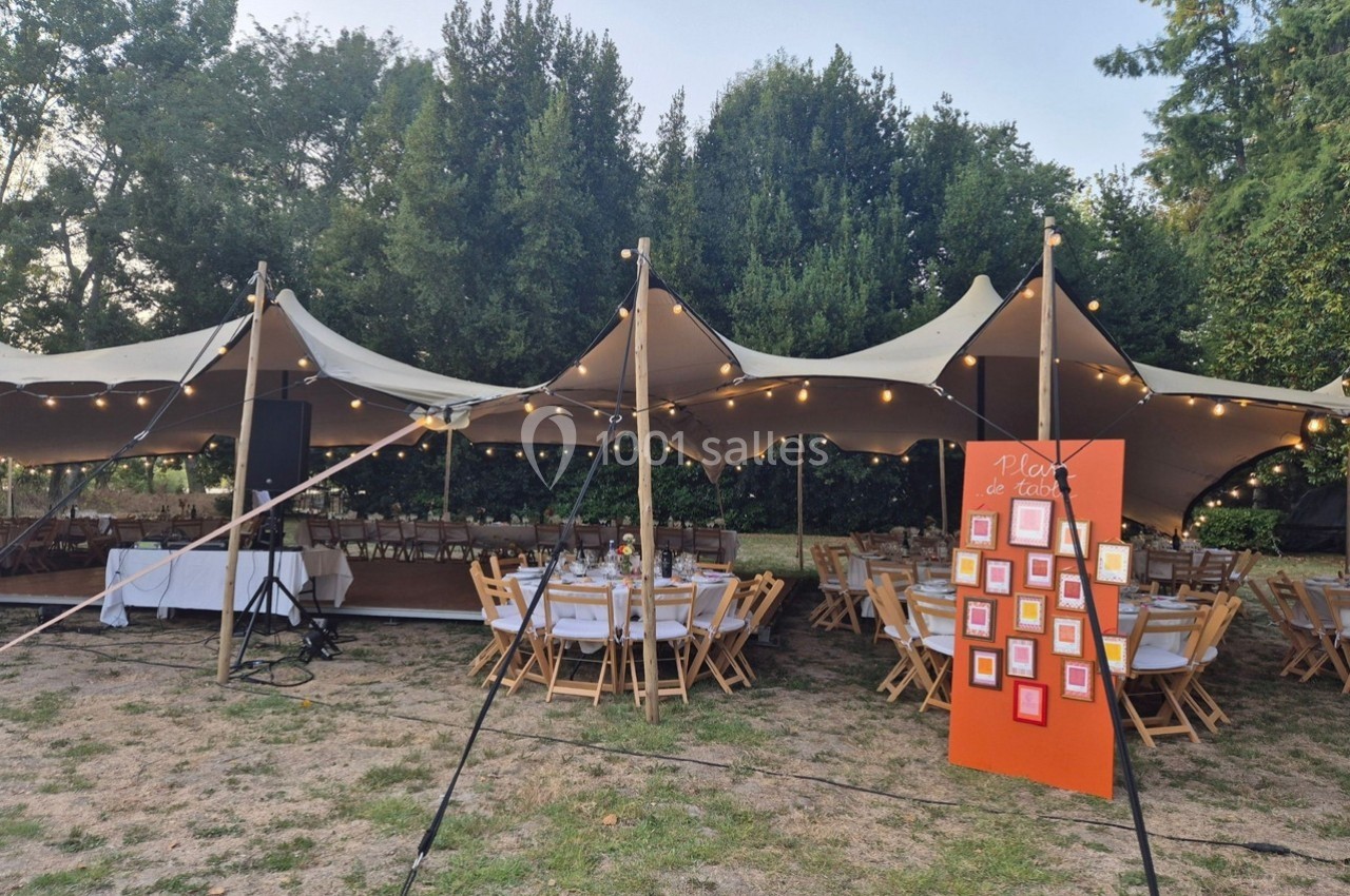 Tente extérieure éclairée abritant des tables dressées pour un événement, avec un plan de table orange au premier plan.