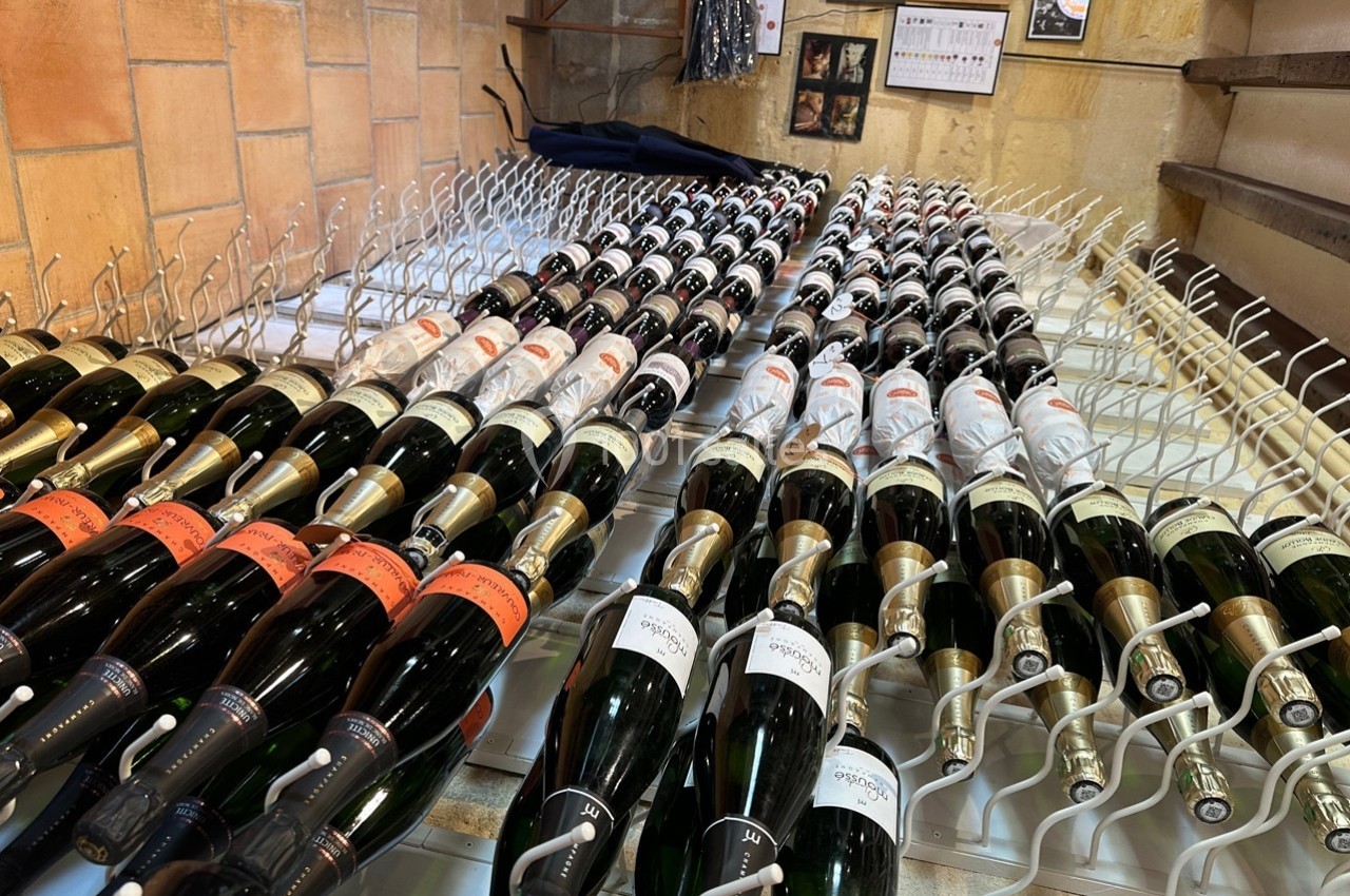 Bouteilles de vin alignées horizontalement sur des supports métalliques dans un espace intérieur aux murs en pierre.