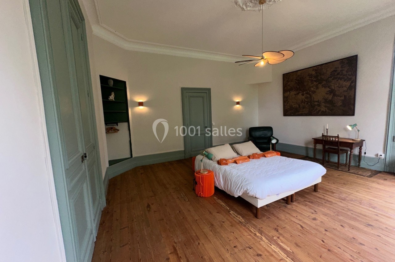 Chambre lumineuse avec parquet en bois, lit double, bureau, fauteuil et décorations murales dans un style épuré.