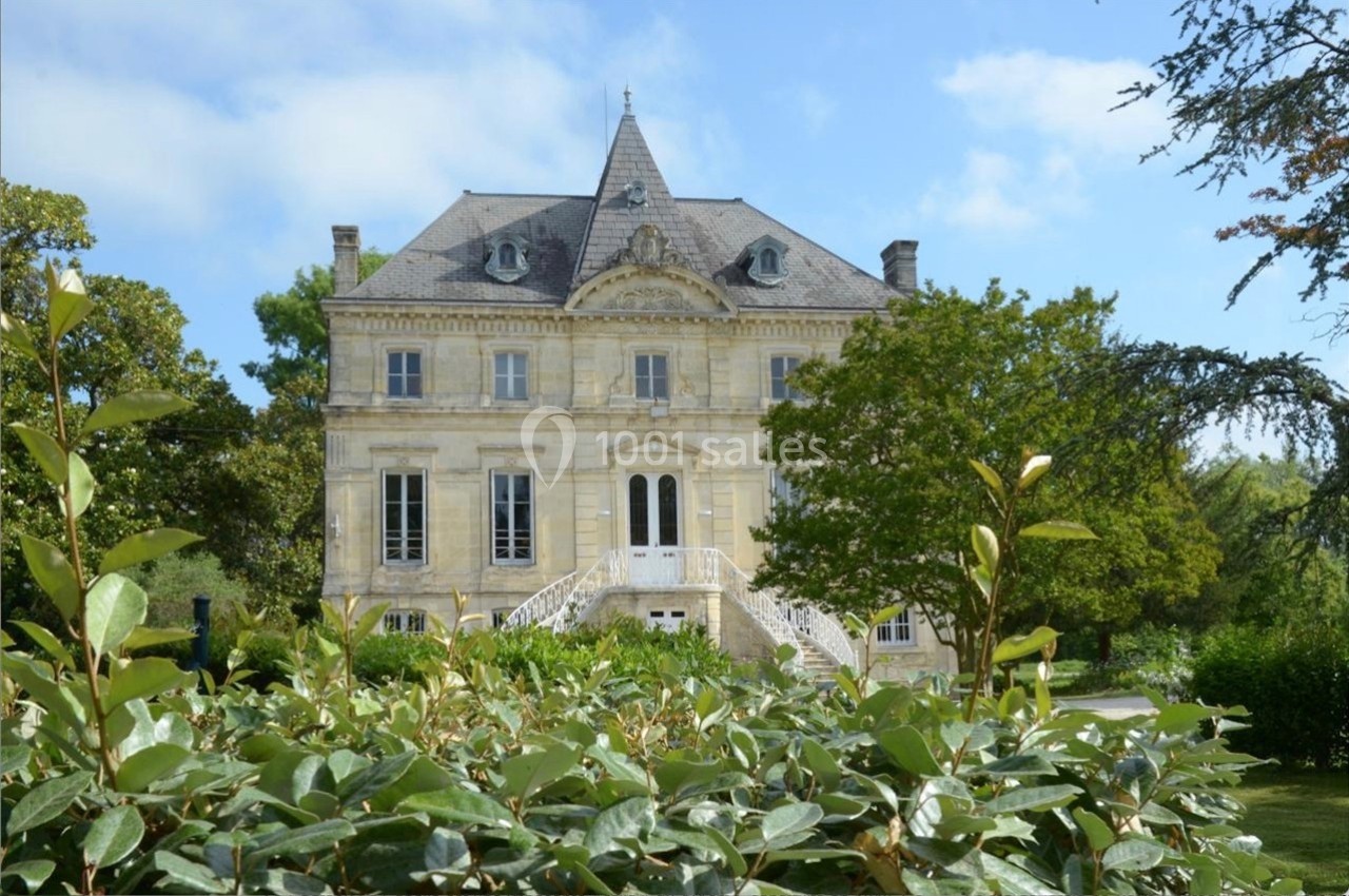 Façade d'un manoir en pierre entouré de verdure, avec un ciel bleu en arrière-plan.