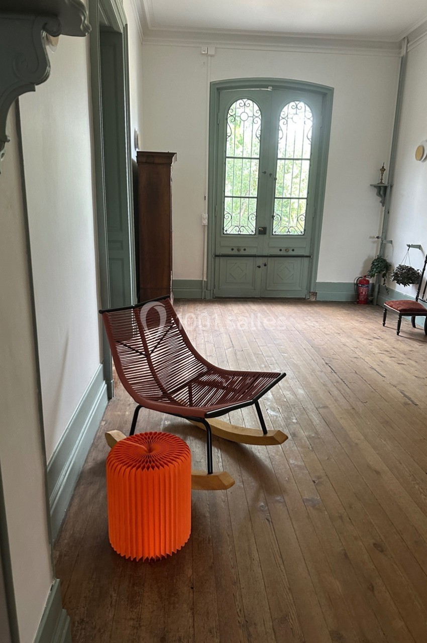 Chaise à bascule en bois et métal avec un tabouret orange dans un couloir lumineux au sol en parquet.