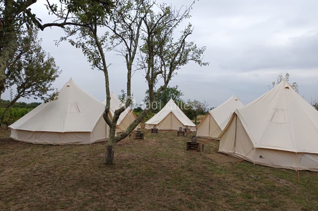 Tentes en toile beige installées sur un terrain herbeux entouré d'arbres par temps nuageux.