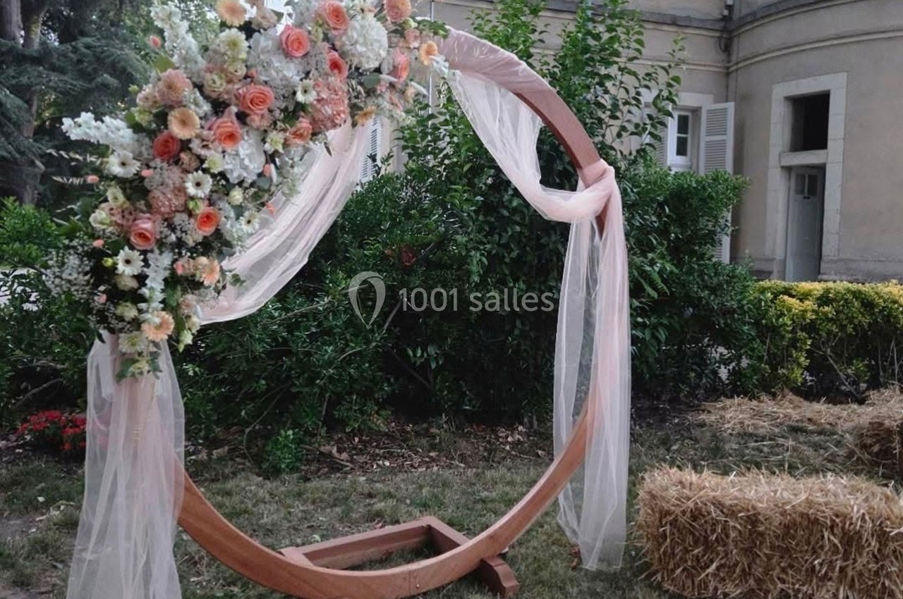 Arche circulaire en bois décorée de fleurs et de voiles, placée dans un jardin près de bottes de paille.