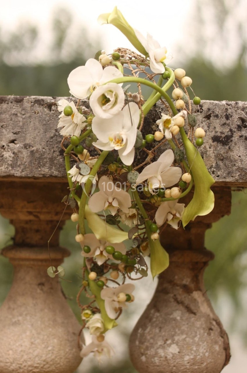 Composition florale avec des orchidées blanches et des feuillages verts, disposée sur une balustrade en pierre.