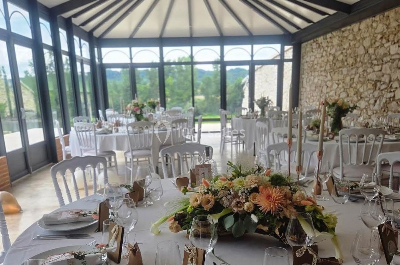 Salle lumineuse avec tables décorées pour un événement, ornées de fleurs et de vaisselle élégante, vue sur l'extérieur…
