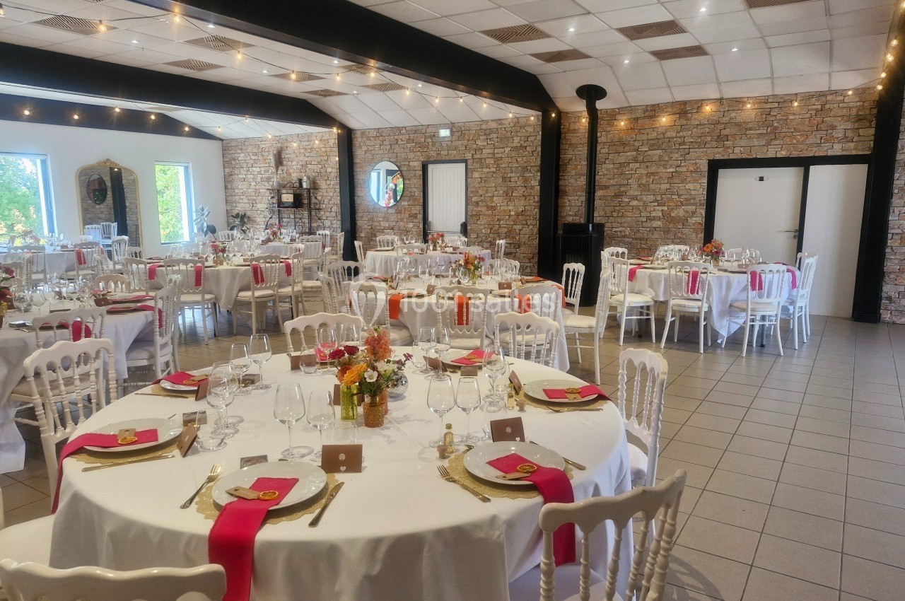 Salle de réception décorée avec des tables rondes, nappes blanches, chemins de table roses et vaisselle élégante.