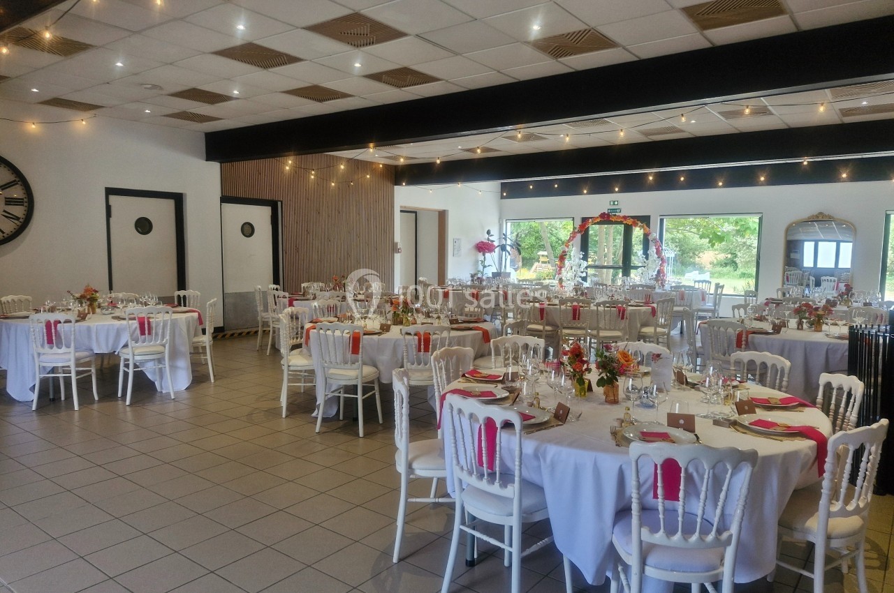 Salle de réception décorée pour un événement, avec des tables rondes dressées et ornées de fleurs colorées.