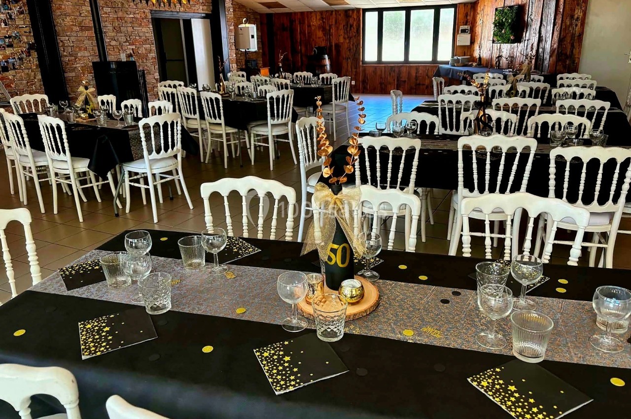 Salle décorée pour une fête, avec tables noires ornées de chemins de table scintillants et une décoration marquant un 50e…