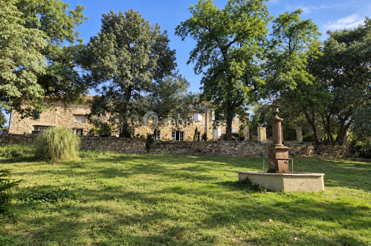 Jardin verdoyant avec une fontaine en pierre au premier plan, bordé d'arbres et d'un bâtiment en pierre à l'arrière-plan.