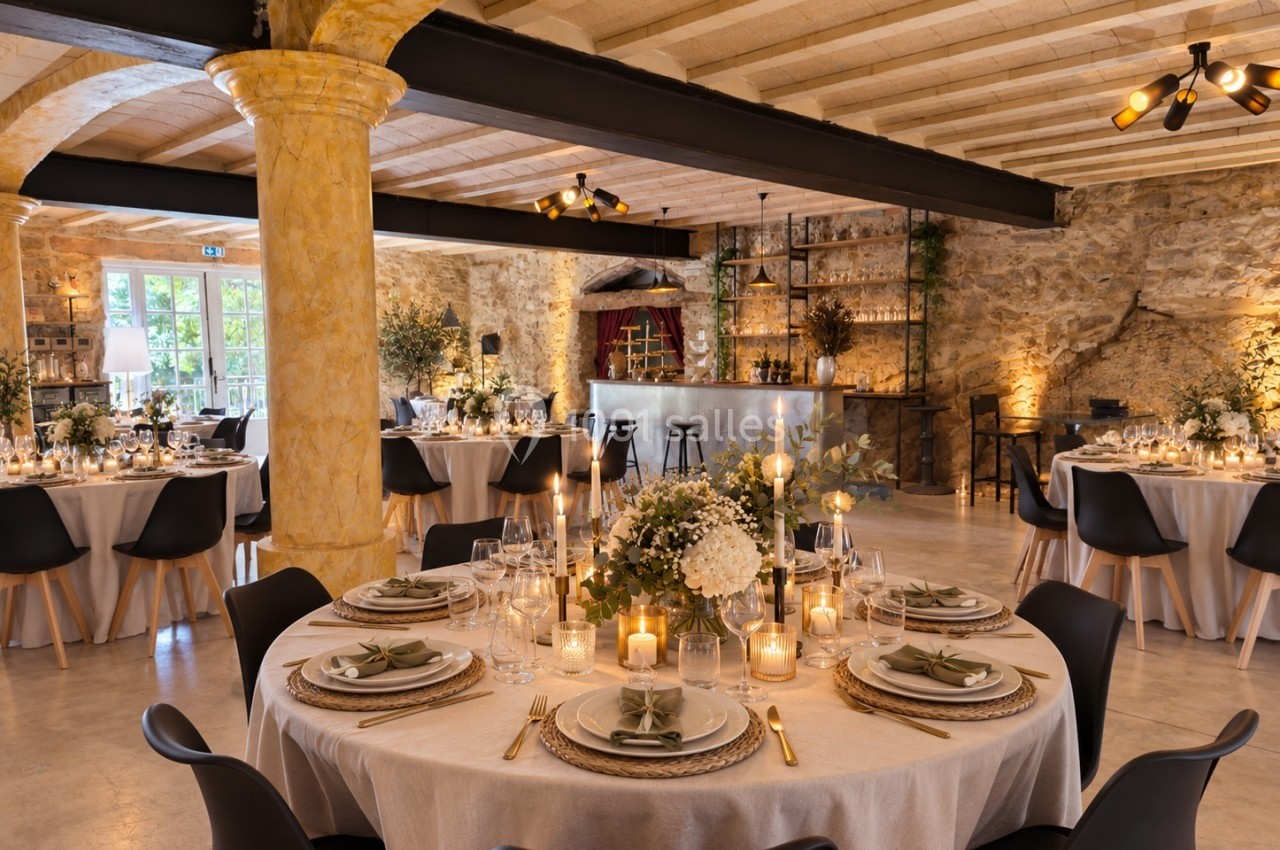 Salle de réception élégante avec tables rondes décorées de bougies, fleurs et vaisselle raffinée, ambiance chaleureuse.