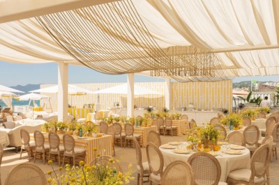 Chaises en rotin entourées de pampas et de décorations jaunes, sous un parasol blanc dans un cadre lumineux.